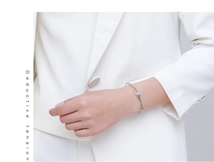 Detail of silver wavy bangle with clover flower charm on a model's wrist