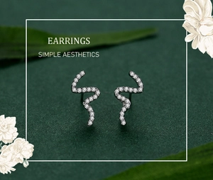 Detailed view of silver snake-shaped earrings with sparkling cubic zirconia on green background