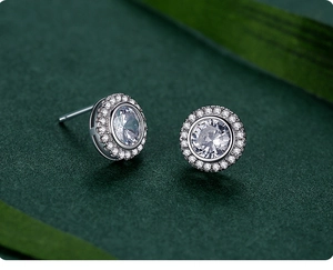 Macro shot of silver halo stud earrings with round brilliant-cut zircon on green leaf