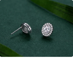 Macro shot of oval halo silver stud earrings with sparkling cubic zirconia on green background