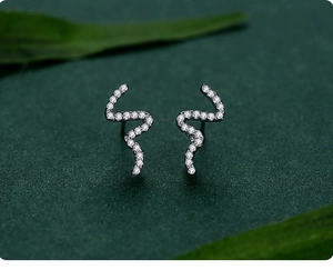 Detailed view of silver snake stud earrings with sparkling cubic zirconia on green foliage