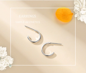Détail des boucles d'oreilles en argent 925 en forme de C sur fond floral minimaliste