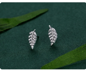 Macro view of S925 silver leaf stud earrings with pavé crystals on a green leaf background