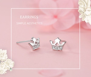 Detailed view of silver crown earrings with sparkling zircons on soft pink background