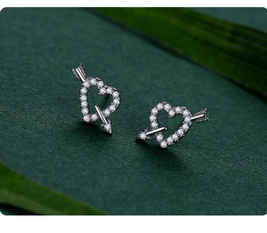 Macro shot of S925 silver heart earrings with micro-inlaid zircons on green leaves