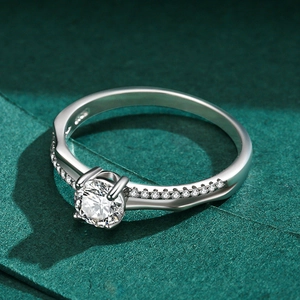 Bague en argent s925 avec solitaire rond à quatre griffes sur une surface vert foncé