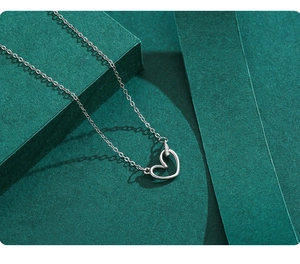 Gros plan du collier coeur évidé en argent S925 avec zircons sur fond texturé vert