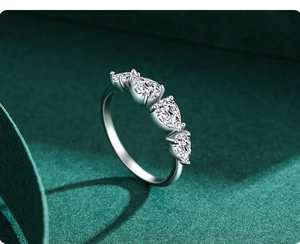 Macro shot of silver ring with five pear-cut stones in claw setting on green background