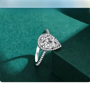 Macro detail of pear-cut 3ct halo ring on dark green velvet luxury display box