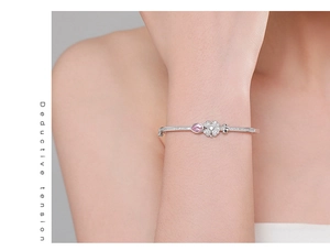 Close-up of a silver clover bracelet featuring a pink teardrop stone on a model's wrist