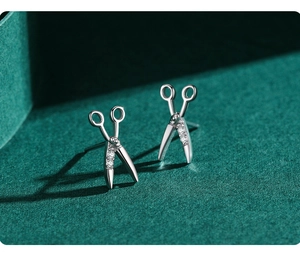 Macro shot of silver scissors stud earrings with white zircon on dark green background