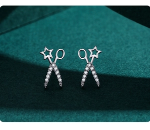 Macro shot of silver scissors earrings with sparkling stars on green velvet base