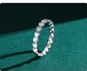 Detail of silver heart rings with paved crystals on a dark green velvet texture