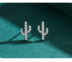 Detailed view of silver cactus stud earrings with micro-set crystals on green velvet