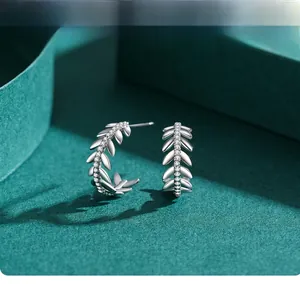Macro shot of silver leaf earrings with white zircons on a dark green background