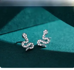 Macro shot of silver snake earrings with sparkling cubic zirconia on green background