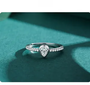 Macro shot of pear-cut sparkling diamond ring in silver setting on green velvet