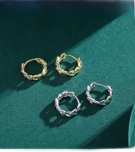 Dettaglio di orecchini a catena oro e argento con zirconi su sfondo verde scuro