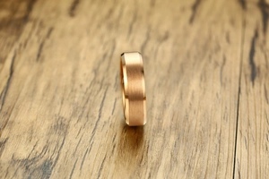 Macro shot of 6mm brushed rose gold tungsten ring with polished edges on wood base