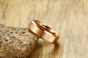 Macro detail of 6mm rose gold brushed tungsten ring resting on natural rock
