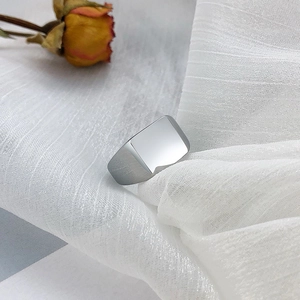 Gros plan d'une bague chevalière carrée en argent sur un tissu blanc avec une rose