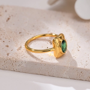 Gold geometric ring with emerald green zircon on travertine stone background
