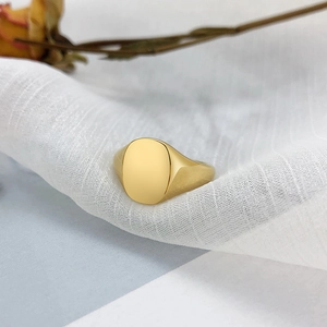Polished gold oval signet ring resting on white textured fabric with a dried rose