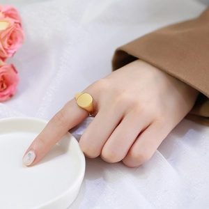 Detail view of a gold signet ring on a model hand with elegant floral background
