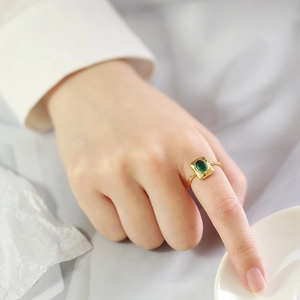 Detailed view of a gold-plated geometric ring featuring a green zircon gemstone on a hand