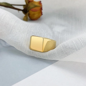 Gros plan d'une bague chevalière carrée dorée sur un tissu blanc texturé élégant