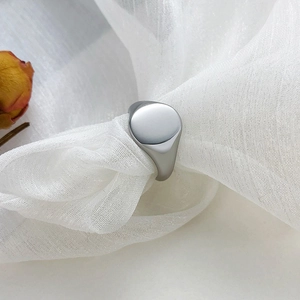Macro shot of minimalist silver oval signet ring on white organza with dried flower petal