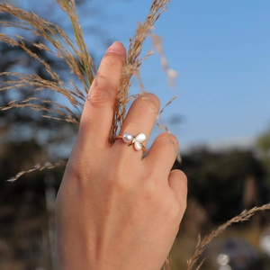 Close-up of adjustable gold shell and pearl ring on finger with sunny outdoor backdrop