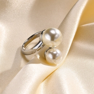 Macro detail of silver-tone ring with dual white pearls on champagne silk fabric
