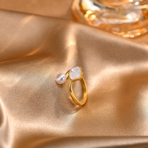 Detail of adjustable gold ring featuring a white pearl and scalloped shell on satin