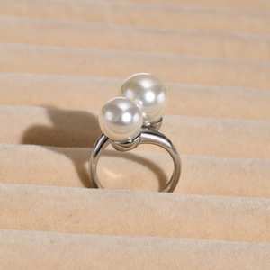 Detailed macro view of an open silver pearl ring with two white round pearls on beige velvet
