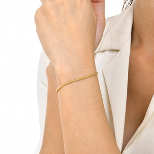 Close-up of a minimalist golden snake chain bracelet worn on a wrist against a white blazer
