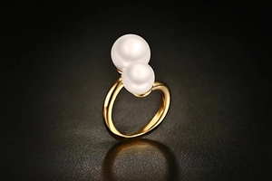 Detailed view of gold pearl open ring featuring two white pearls on a textured background