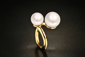 Detail of gold titanium steel open ring featuring two white pearls on a dark surface