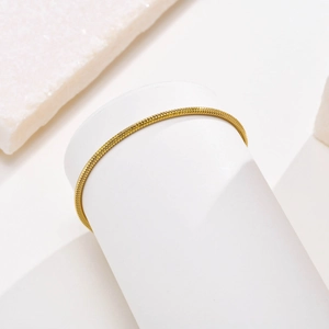 Detailed view of a gold snake chain bracelet elegantly wrapped around a white display stand