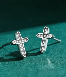 Vue macro de boucles d'oreilles croix en argent avec oxydes de zirconium sur fond vert
