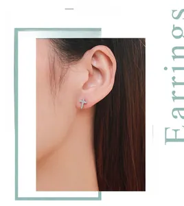 Gros plan d'un clou d'oreille croix en argent S925 serti de zircons porté par une femme