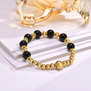 Detail of beaded bracelet with black natural stones and gold steel beads on white layers
