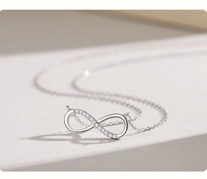 Macro shot of silver infinity pendant with pavé diamonds on a minimalist beige base