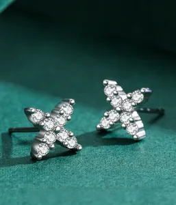 Macro shot of silver X-shaped earrings with zircon pave setting on green background