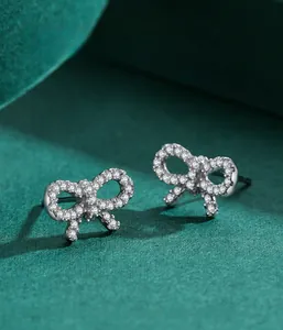 Macro shot of silver bow earrings with pavé white zircons on a dark green background