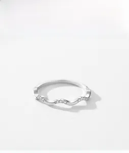 Macro detail of silver wavy ring with small zircons on textured white background