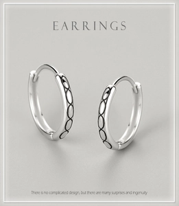 Macro view of silver hoop earrings featuring polished oval geometric engravings