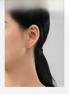Close-up of minimalist polished silver heart stud earring worn on model's ear