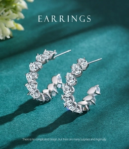 Macro view of C-shaped silver earrings with pear-cut crystals on green velvet