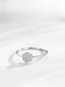 Détail d'une bague fleur en argent S925 avec micro-diamants sur tissu blanc doux